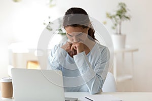 Gloomy young woman sitting at desk looking at computer screen