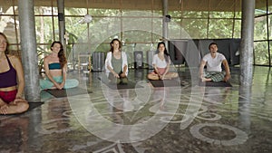 Mixed race group sit in a circle on their yoga mats ready to follow a sound healing meditation in Thailand