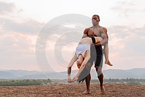 Mixed race gymnastic couple with perfect muscular bodies in sportswear dancing on mountains landscape background. Pink