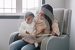 Mixed race Indian mom reading book with African black baby girl toddler at home. Early age children education and development. photo