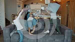 Mixed race lady nanny playing pillow fight with children laughing having fun indoors