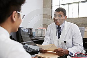 Mixed race male doctor holding documents in patient meeting