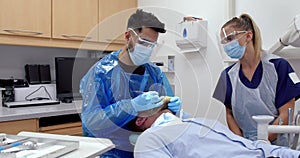 Mixed race male nurse dressed in surgical gear with female dentist holding tools before operating on male patient