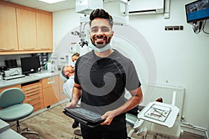 Mixed race male nurse standing holding digital tablet standing in doctors office with patient and female dentist holding