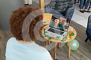 Mixed race man at bar making st patrick\'s day video call to friend on laptop