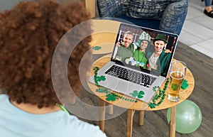 Mixed race man at bar making st patrick\'s day video call to friends in costumes smiling on laptop