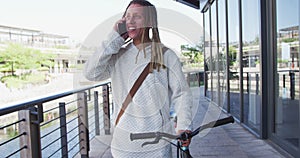 Mixed race man with dreadlocks wheeling a bicycle in the street talking on smartphone