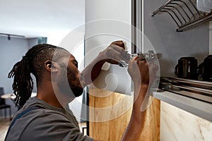 Mixed-race man fixing white cupboard door using spanner
