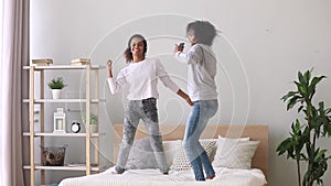Mixed race mother and daughter enjoy music dancing on bed