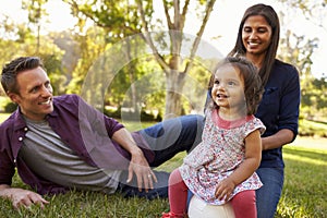 Mixed race parents and young daughter sit in park, close up