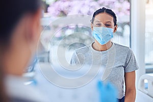 Mixed race patient wearing a mask in consult with a doctor. Doctor checking a patients chart on a clipboard. Doctor