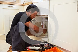 Mixed race plumber fixing the kitchen sink in a home