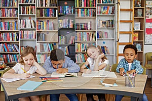 Mixed-race pupils study and write at table in library or classroom. Back to school