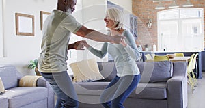 Mixed race senior couple dancing together in the living room at home