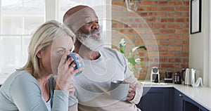 Mixed race senior couple drinking coffee together in the kitchen at home