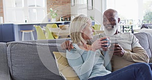 Mixed race senior couple drinking coffee together while sitting on the couch at home