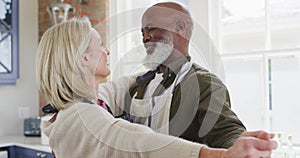 Mixed race senior couple wearing aprons dancing together in the kitchen at home