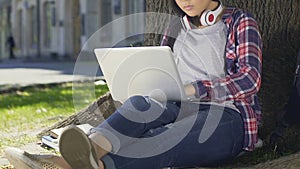 Mixed-race student doing her diploma project sitting with laptop openair