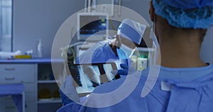 Mixed race surgeons wearing protective clothing looking at lung x-ray on tablet in operating theatre