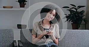 Mixed race teenager girl sitting in room on couch resting, surfing Internet, making date online, texting with her