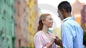 Mixed-race teenager tenderly holding hand of girl saying compliments, date