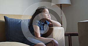 Mixed race thoughtful girl, sitting on soda in living room