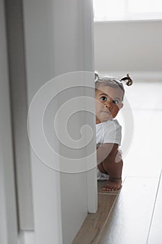 Mixed race toddler girl playing and hiding behind the opened door in room