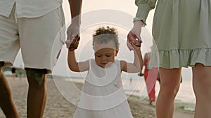 Mixed race toddler girl walks with mom and dad at seaside