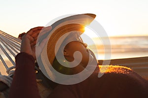 Mixed race woman on beach holiday lying in hammock relaxing during sunset