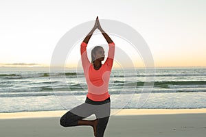 Mixed race woman on beach practicing yoga at sunset