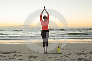 Mixed race woman on beach practicing yoga during sunset