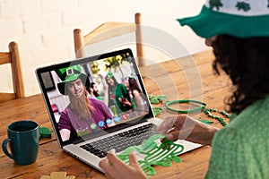 Mixed race woman in costume making st patrick\'s day video call to friends on laptop at home