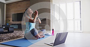 Mixed race woman excercising on a mat with laptop