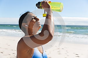 Mixed race woman exercising on beach wearing wireless earphones dousing with water