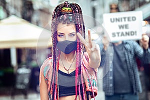 Mixed race woman with face mask showing peace sign during street protest