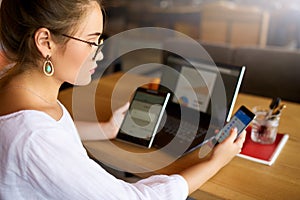 Mixed race woman in glasses working with multiple electronic internet devices. Freelancer businesswoman has tablet and