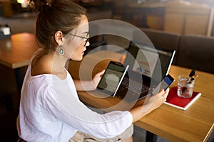 Mixed race woman in glasses working with multiple electronic internet devices. Freelancer businesswoman has tablet and photo