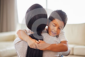 Mixed race woman hugging her adorable little son on the while bonding together at home. Small hispanic boy smiling and