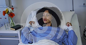 Mixed race woman lying in hospital bed fluffing her pillow