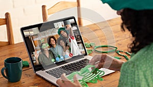 Mixed race woman making st patrick's day video call to diverse group of friends on laptop at home