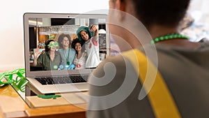 Mixed race woman making st patrick's day video call to diverse group of friends on laptop at home