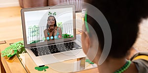 Mixed race woman making st patrick's day video call to female friend blowing kiss on laptop at home