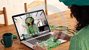 Mixed race woman making st patrick's day video call to female friend in costume on laptop at home