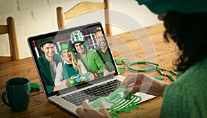 Mixed race woman making st patrick\'s day video call to happy friends in costumes on laptop at home