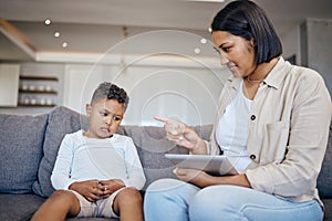 Mixed race woman pointing to scold and discipline her little son about internet use on digital tablet at home. Naughty