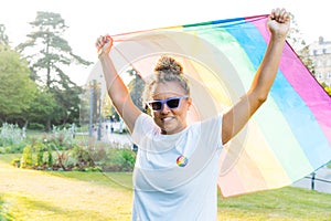 Mixed race woman raising a rainbow flag outdoor. Young lesbian activist smiling and holding flag symbol of social movement Lgbtq. photo
