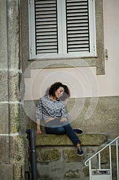 A mixed-race woman sitting near the wall of the house in Porto