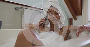 Mixed race woman taking a bath and talking on smartphone