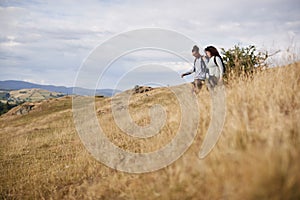A mixed race young adult couple smile while walking across a field downhill during a mountain hike