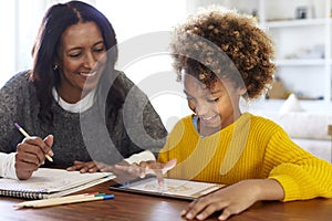 African American  young grandmother sitting at table doing homework with her granddaughter using a tablet computer, close up